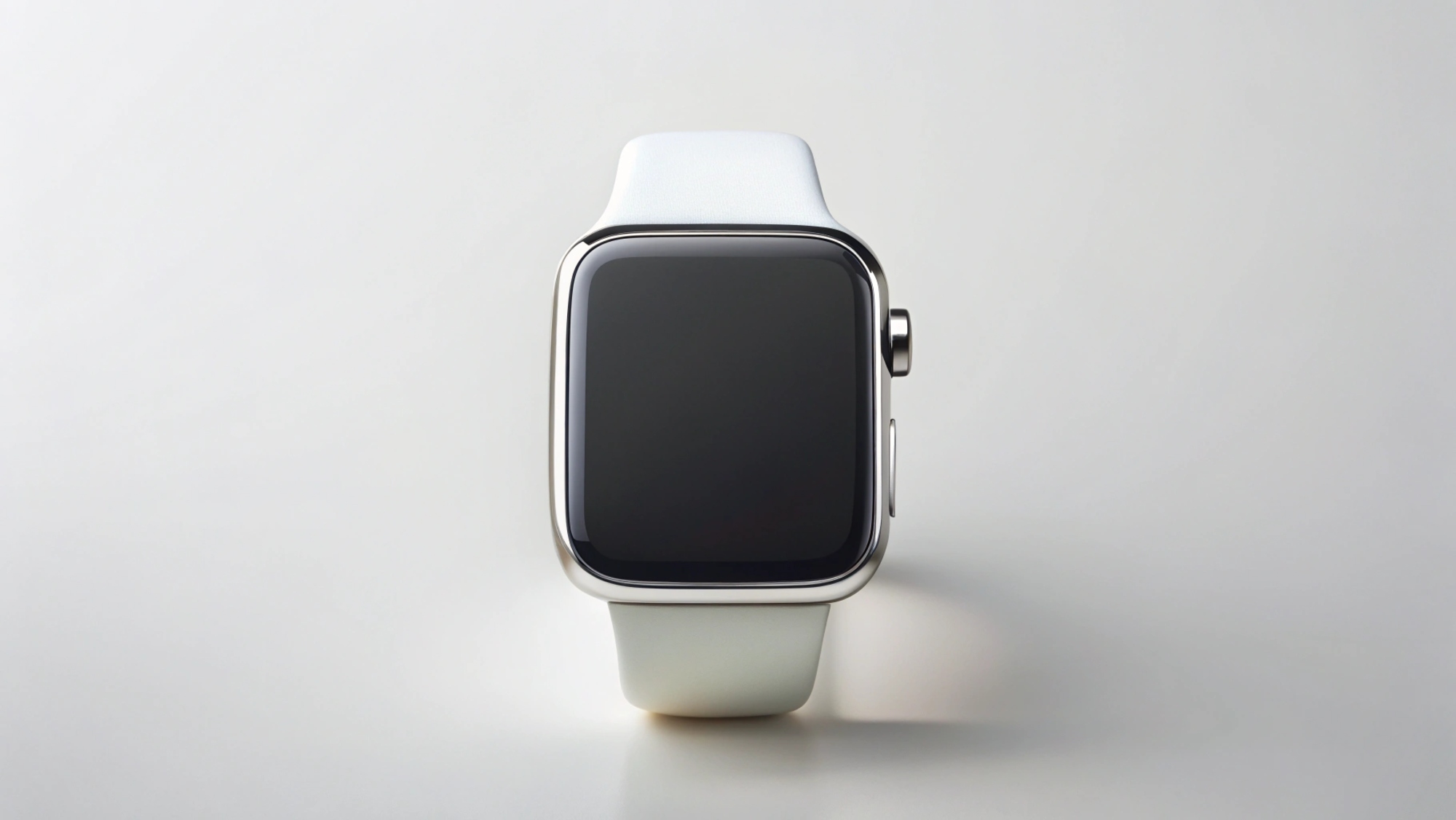 На изображении показаны смарт-часы Apple Watch SE 2020 из алюминия с прямоугольным корпусом и белым ремешком, расположенные в центре кадра. Экран часов чёрный. Корпус часов имеет серебристый цвет. Справа от экрана находится кнопка. Поверхность под часами светлая и однотонная. Освещение ровное и рассеянное.